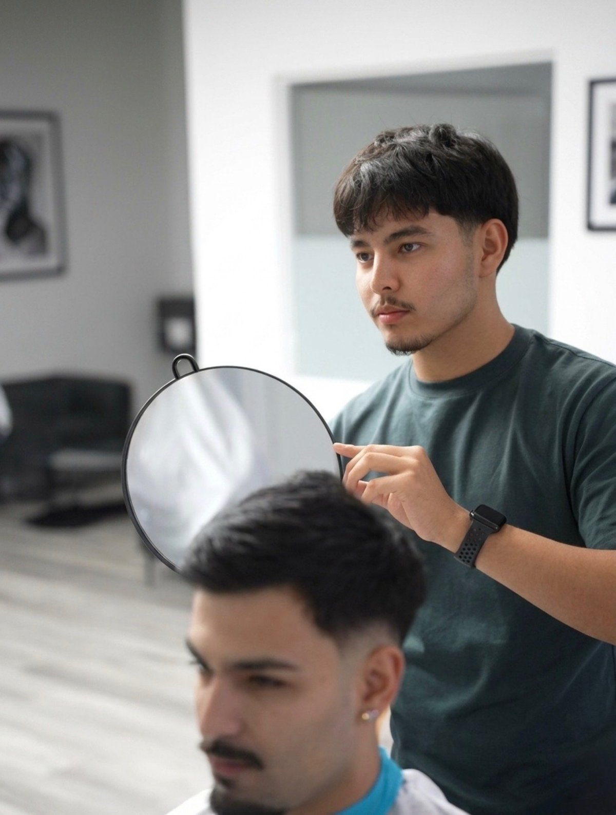 Barber holding mirror behind clients head in salon, showing finished haircut